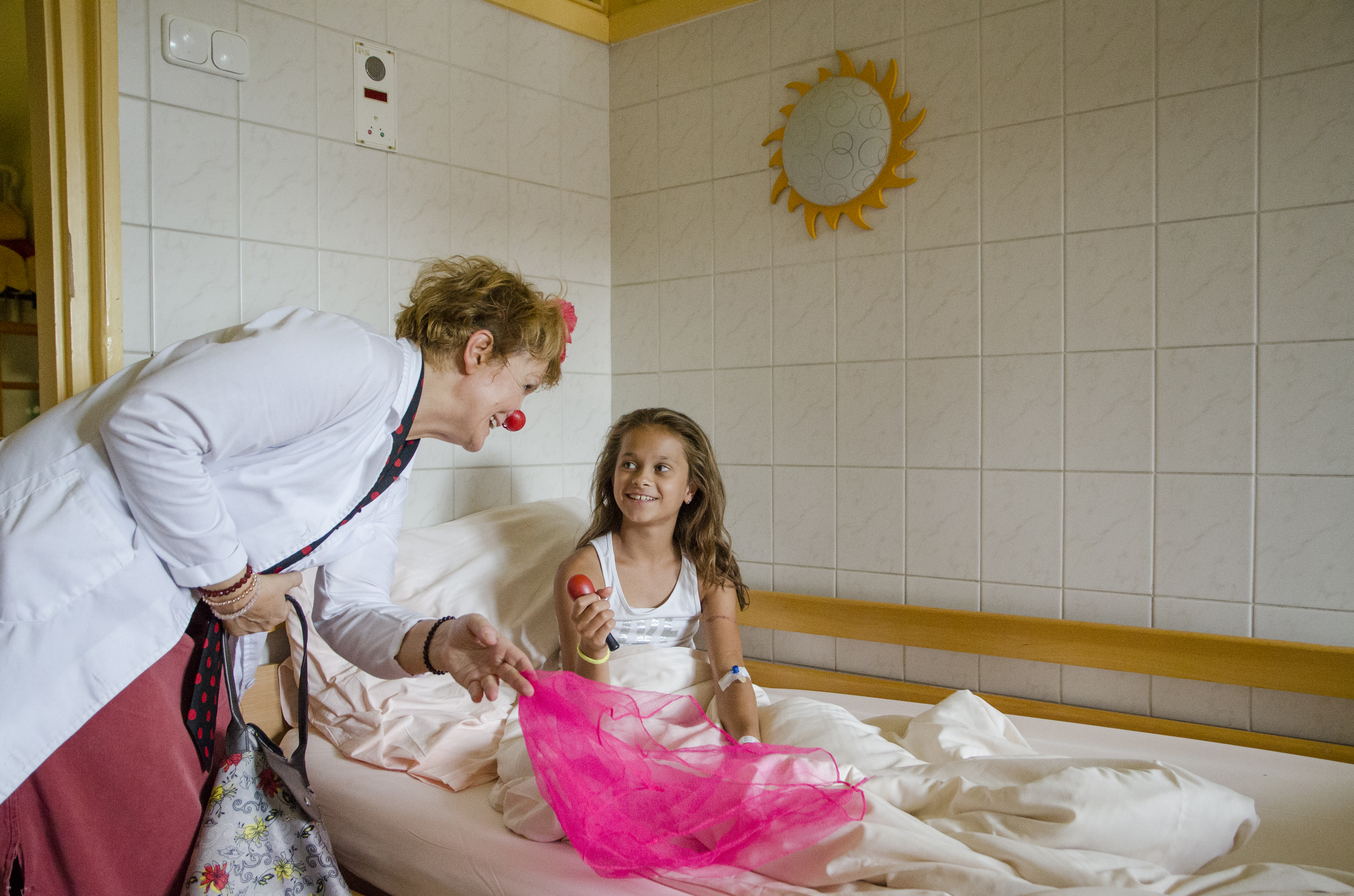 Bohócdoktor színes kendővel a gyermek kórházi ágyánál