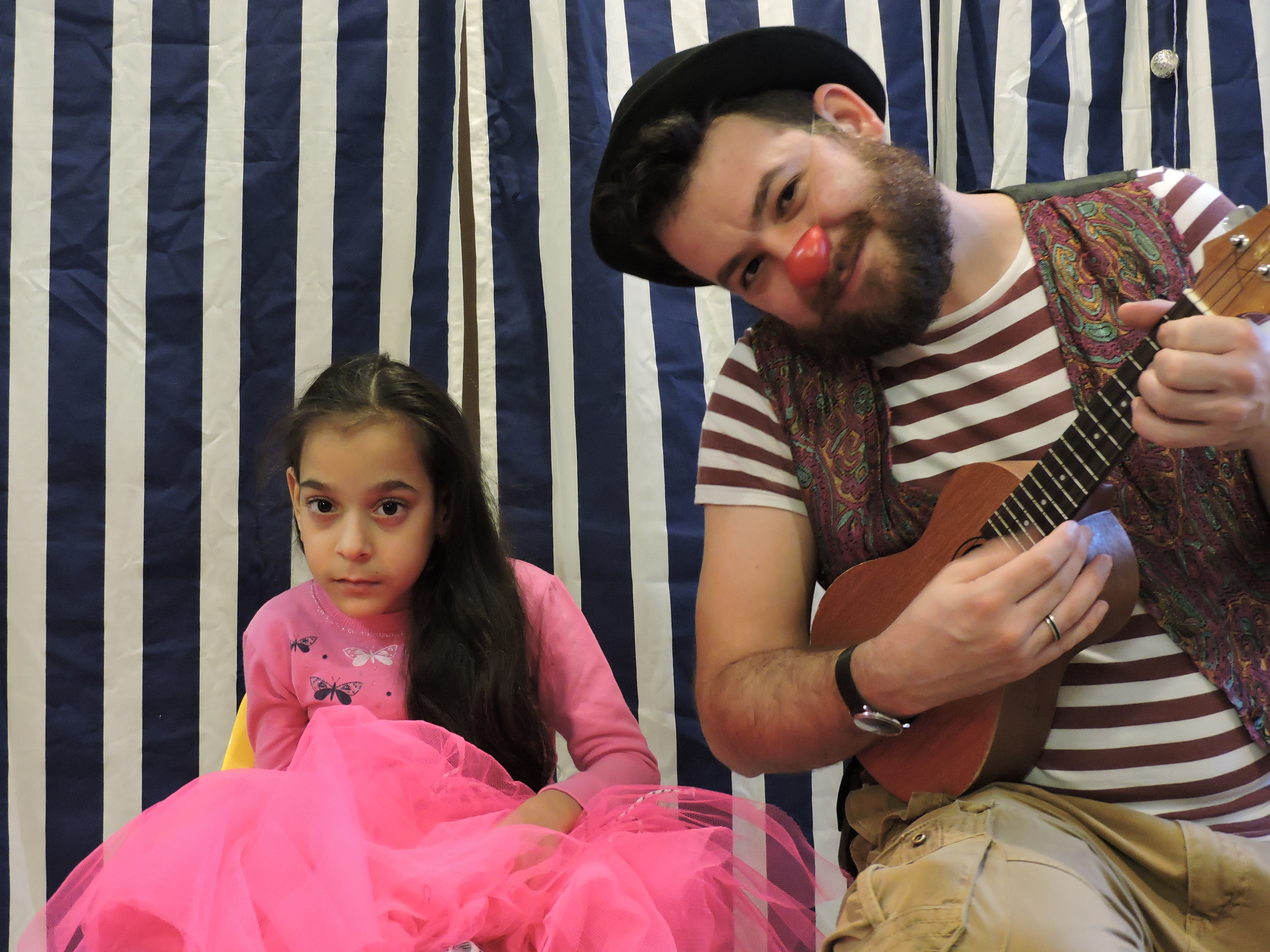 Bohócdoktor ukulelével zenél egy kislánynak